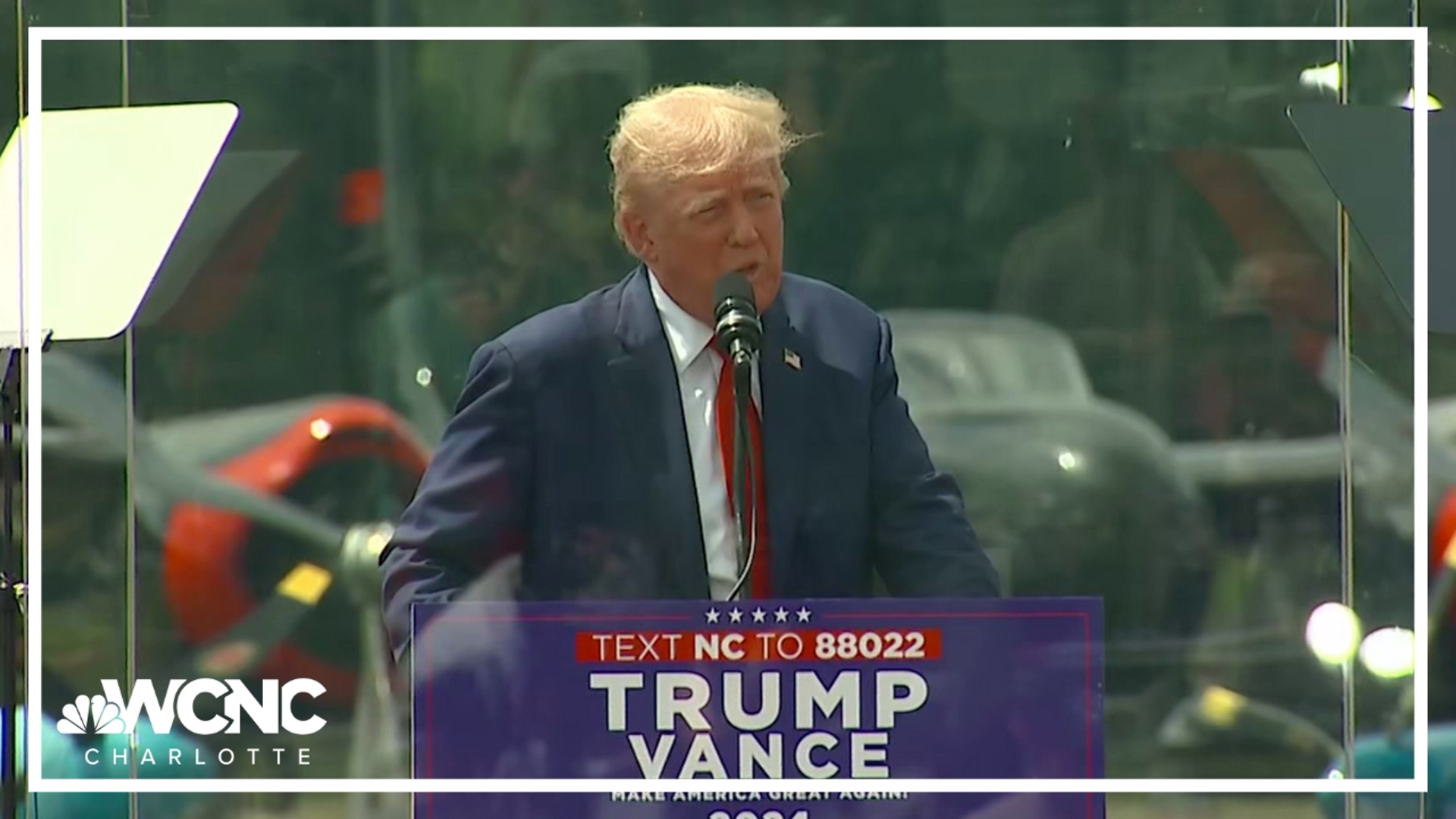 Trump’s podium at the North Carolina Aviation Museum & Hall of Fame is surrounded by panes of bulletproof glass that form a protective wall across the stage.